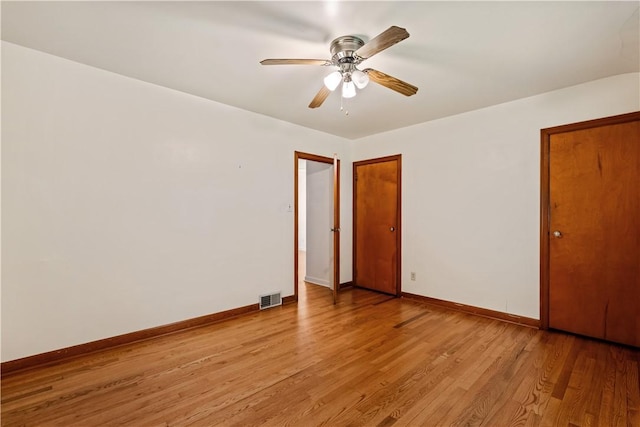 empty room with light wood finished floors, baseboards, a ceiling fan, and visible vents