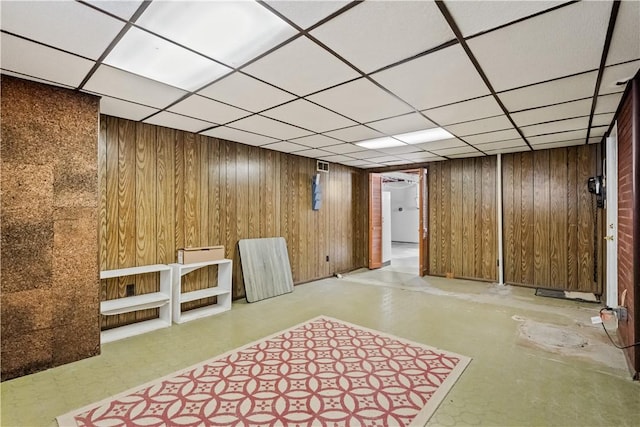 finished basement with wooden walls, visible vents, and a drop ceiling