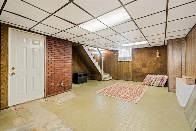 basement featuring stairway, wood walls, and a paneled ceiling