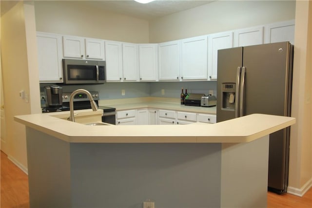 kitchen with a sink, white cabinetry, light wood-style floors, light countertops, and appliances with stainless steel finishes