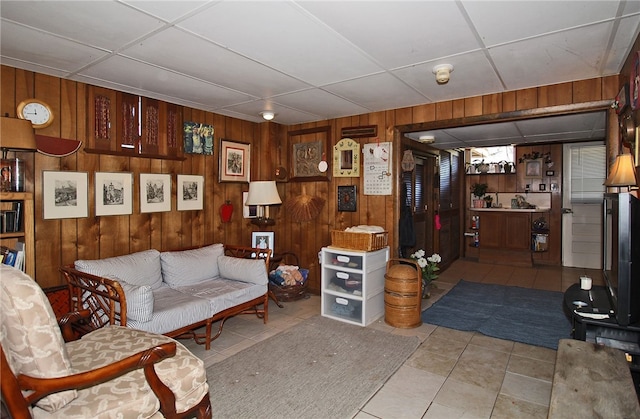 living area with a paneled ceiling, tile patterned flooring, and wood walls