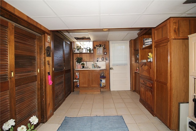 interior space with a drop ceiling, light tile patterned floors, and wood walls