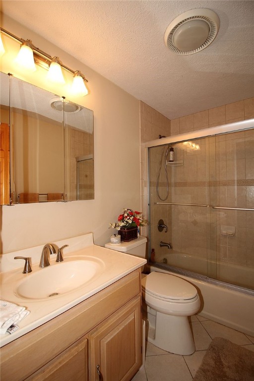 full bathroom with toilet, vanity, a textured ceiling, tile patterned flooring, and shower / bath combination with glass door