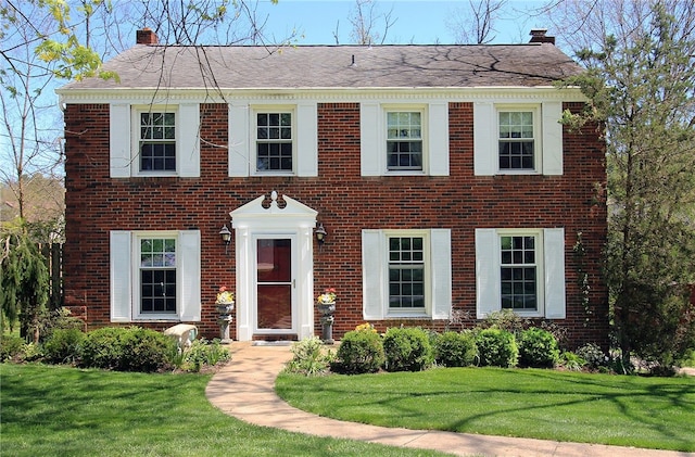 colonial home featuring a chimney and brick siding