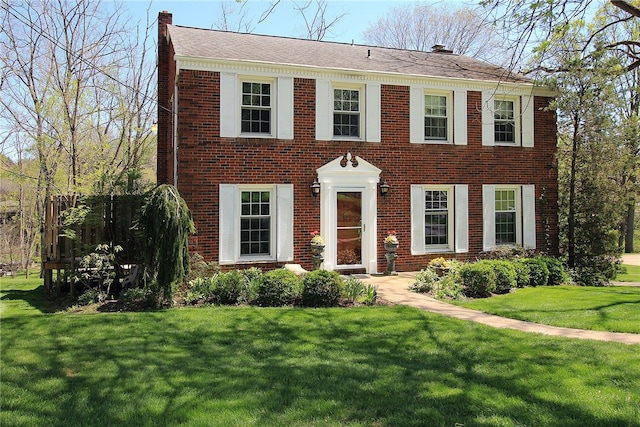 colonial house with a front lawn, brick siding, and a chimney