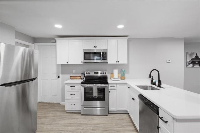 kitchen featuring a sink, a peninsula, stainless steel appliances, light wood finished floors, and light countertops