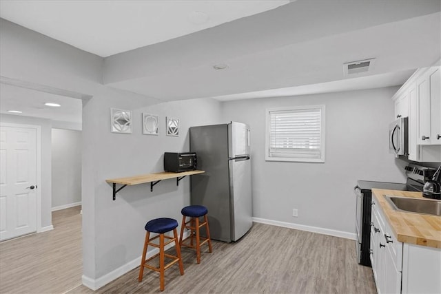 kitchen featuring wood counters, appliances with stainless steel finishes, light wood finished floors, and baseboards