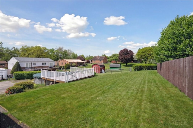 view of yard featuring fence, a storage shed, a wooden deck, and an outdoor structure