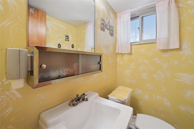 half bath with a sink, toilet, and wallpapered walls