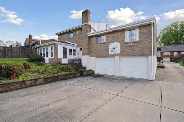 back of house with fence, brick siding, concrete driveway, a garage, and a chimney