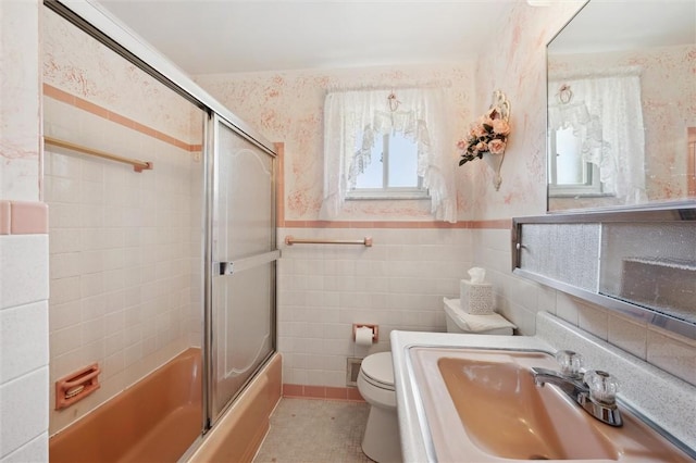 bathroom featuring tile walls, toilet, vanity, shower / bath combination with glass door, and wallpapered walls