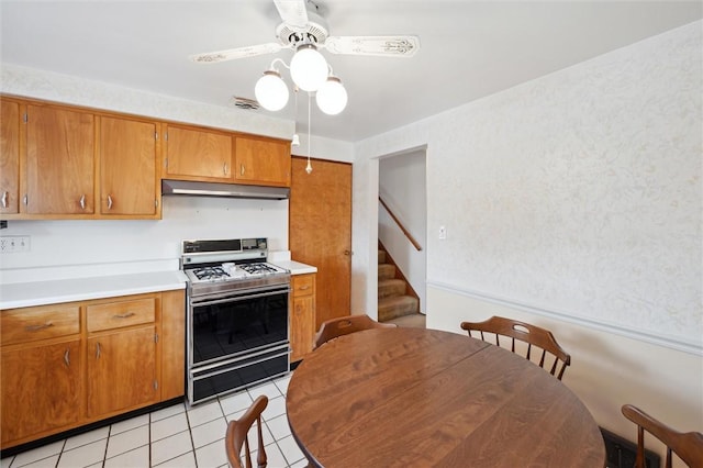 kitchen featuring under cabinet range hood, range with gas stovetop, ceiling fan, brown cabinets, and light countertops