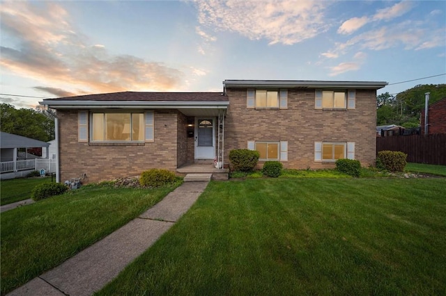 split level home featuring a front lawn, brick siding, and fence