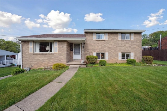split level home featuring fence, brick siding, and a front yard
