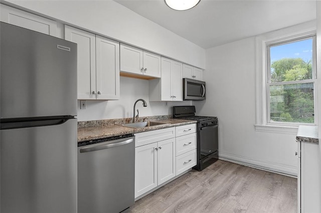 kitchen featuring light wood-style flooring, a sink, white cabinets, baseboards, and appliances with stainless steel finishes
