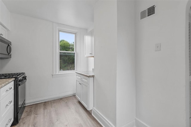 kitchen with visible vents, gas stove, white cabinets, baseboards, and light wood-style floors