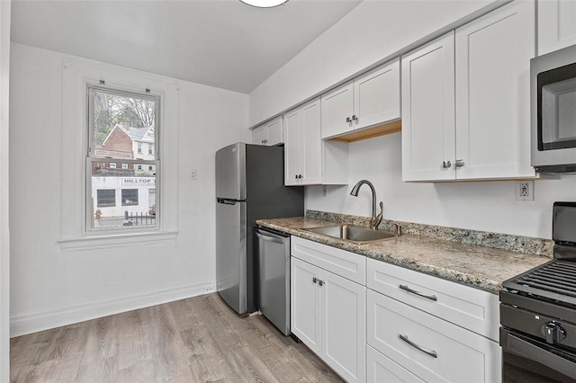 kitchen with light stone countertops, a sink, white cabinetry, light wood-style floors, and appliances with stainless steel finishes