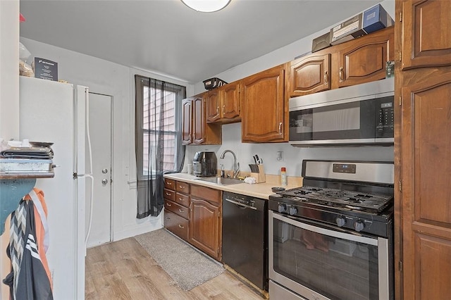 kitchen featuring a sink, stainless steel appliances, brown cabinets, light wood-type flooring, and light countertops