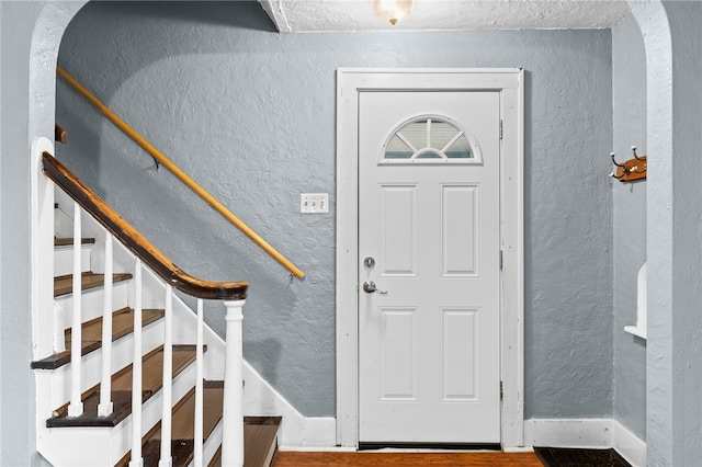 entrance foyer featuring a textured wall, stairway, wood finished floors, and baseboards