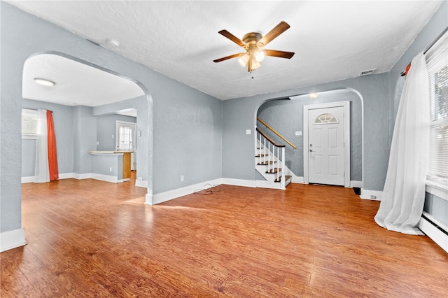 unfurnished living room with arched walkways, a ceiling fan, wood finished floors, stairway, and a textured wall