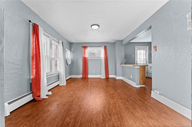 unfurnished room with wood finished floors, a textured wall, a baseboard radiator, and baseboards