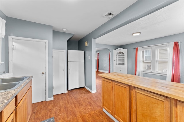 kitchen featuring freestanding refrigerator, wood counters, a sink, light wood-type flooring, and baseboards