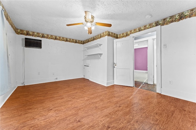 empty room featuring a textured ceiling, wood finished floors, a wall unit AC, a ceiling fan, and baseboards