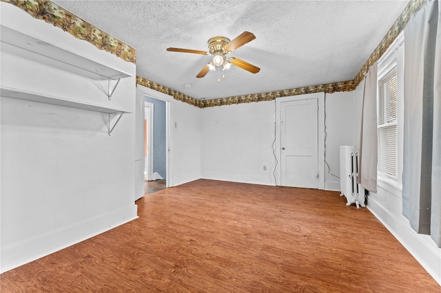 unfurnished room featuring radiator, a textured ceiling, a ceiling fan, wood finished floors, and baseboards