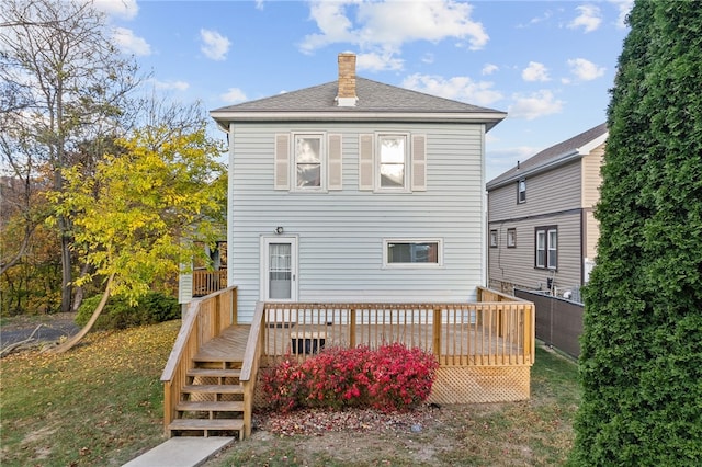 rear view of property with a wooden deck, a chimney, a shingled roof, and a lawn