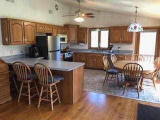 kitchen with freestanding refrigerator, lofted ceiling, a peninsula, and brown cabinets