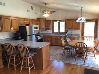 kitchen with a peninsula, stainless steel appliances, brown cabinetry, dark wood-type flooring, and vaulted ceiling