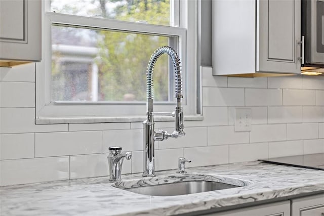 interior details with stainless steel microwave, light stone counters, decorative backsplash, and a sink