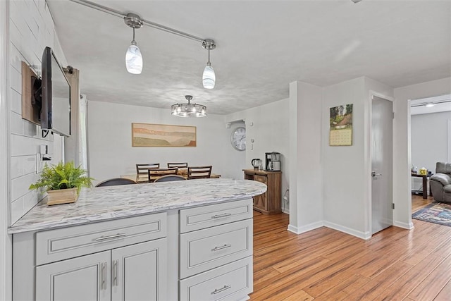 kitchen with a peninsula, light stone counters, light wood finished floors, and baseboards