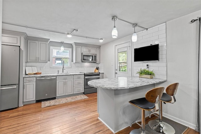kitchen with light wood finished floors, a peninsula, backsplash, stainless steel appliances, and gray cabinets
