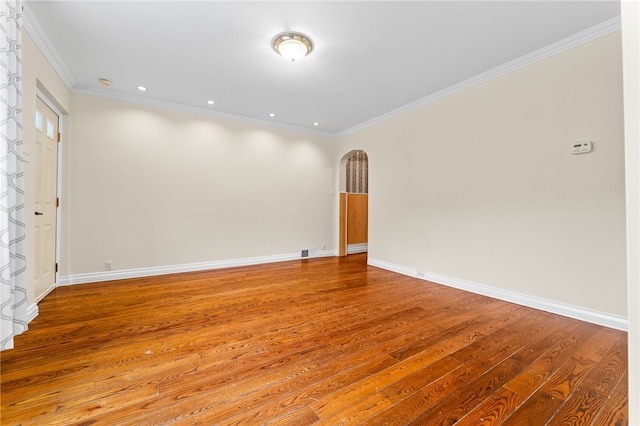 unfurnished room with wood finished floors, ornamental molding, visible vents, arched walkways, and baseboards