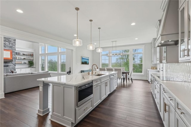 kitchen with glass insert cabinets, a sink, a kitchen island with sink, custom range hood, and recessed lighting