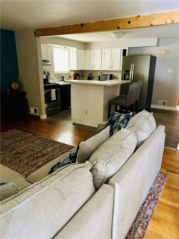 living room with visible vents, wood finished floors, baseboards, and beamed ceiling