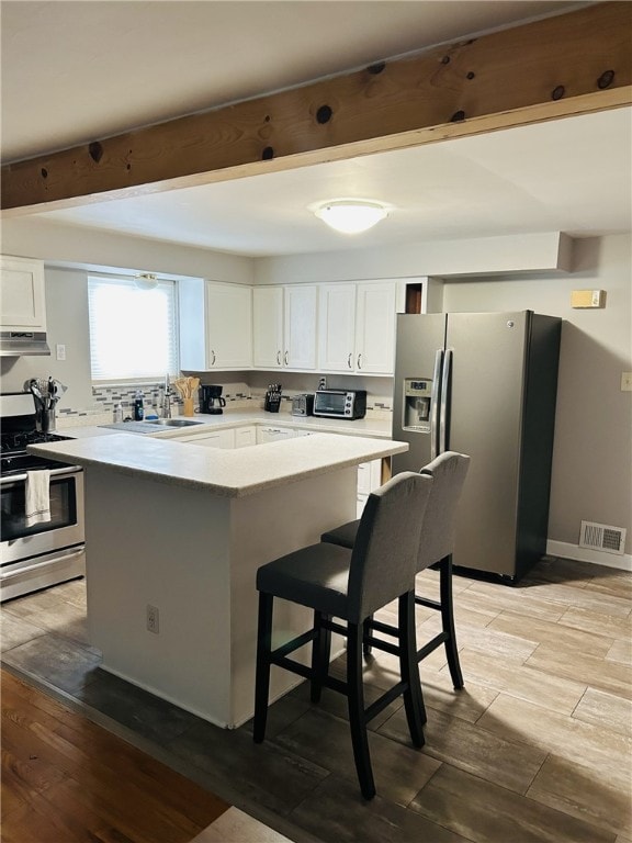 kitchen featuring a sink, beam ceiling, visible vents, under cabinet range hood, and appliances with stainless steel finishes