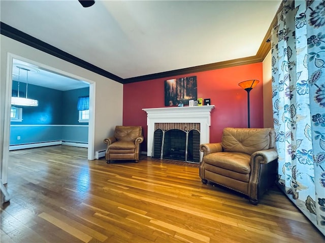 sitting room with a baseboard heating unit, wood finished floors, crown molding, a baseboard radiator, and a brick fireplace