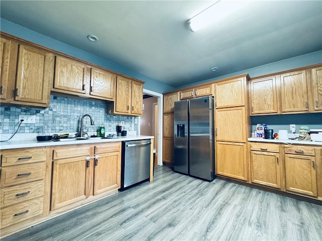 kitchen featuring light wood-style flooring, a sink, stainless steel appliances, backsplash, and light countertops