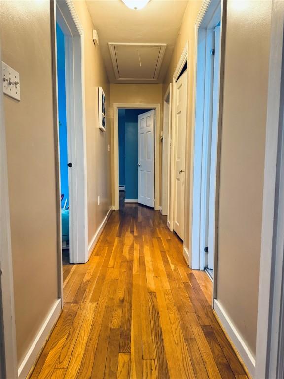 hall with attic access, baseboards, and wood-type flooring