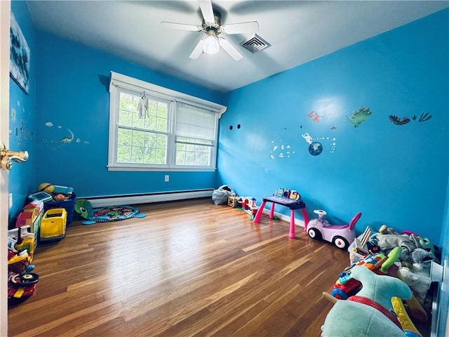 recreation room featuring a baseboard heating unit, ceiling fan, visible vents, and wood finished floors
