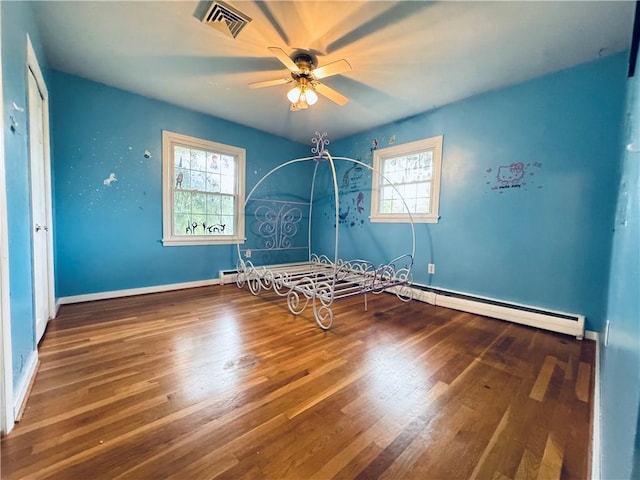 unfurnished bedroom featuring wood finished floors, visible vents, baseboards, ceiling fan, and a baseboard heating unit