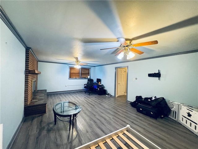 living room featuring wood finished floors, a ceiling fan, a brick fireplace, crown molding, and baseboards