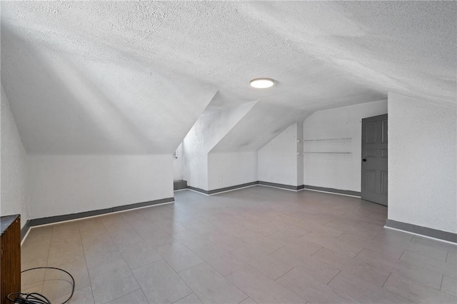 bonus room featuring lofted ceiling, a textured ceiling, and baseboards