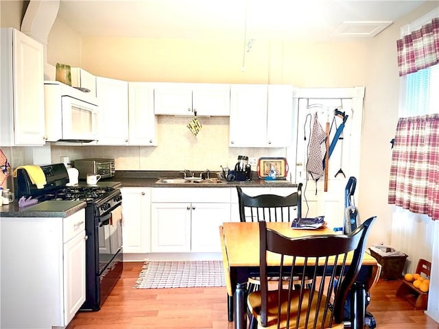 kitchen with a sink, white microwave, black gas stove, dark countertops, and light wood-style floors