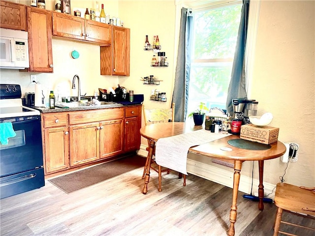 kitchen with a sink, dark countertops, range with electric cooktop, light wood-type flooring, and white microwave