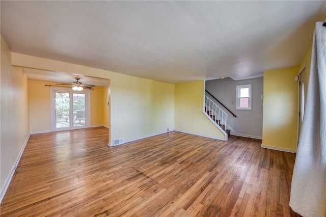 unfurnished living room with light wood-type flooring, visible vents, baseboards, and stairway