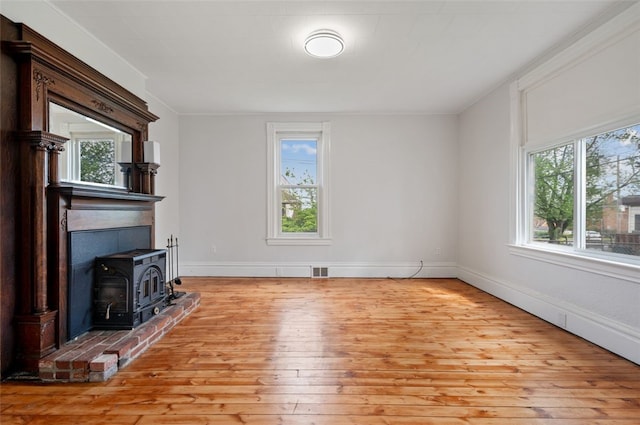unfurnished living room with baseboards, visible vents, crown molding, a wood stove, and hardwood / wood-style floors