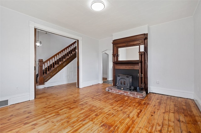 unfurnished living room featuring baseboards, visible vents, stairs, arched walkways, and hardwood / wood-style floors